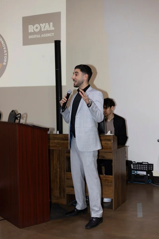 The event host speaking from the front of the room.
